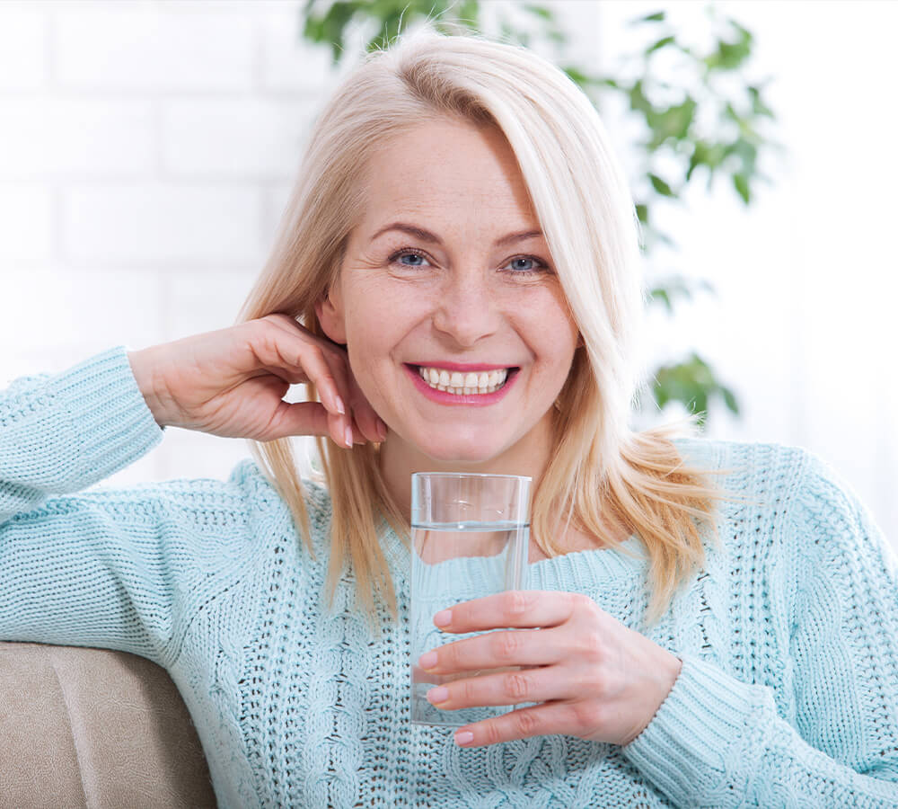 Woman smiling and waiting on the sofa. She drinks water.