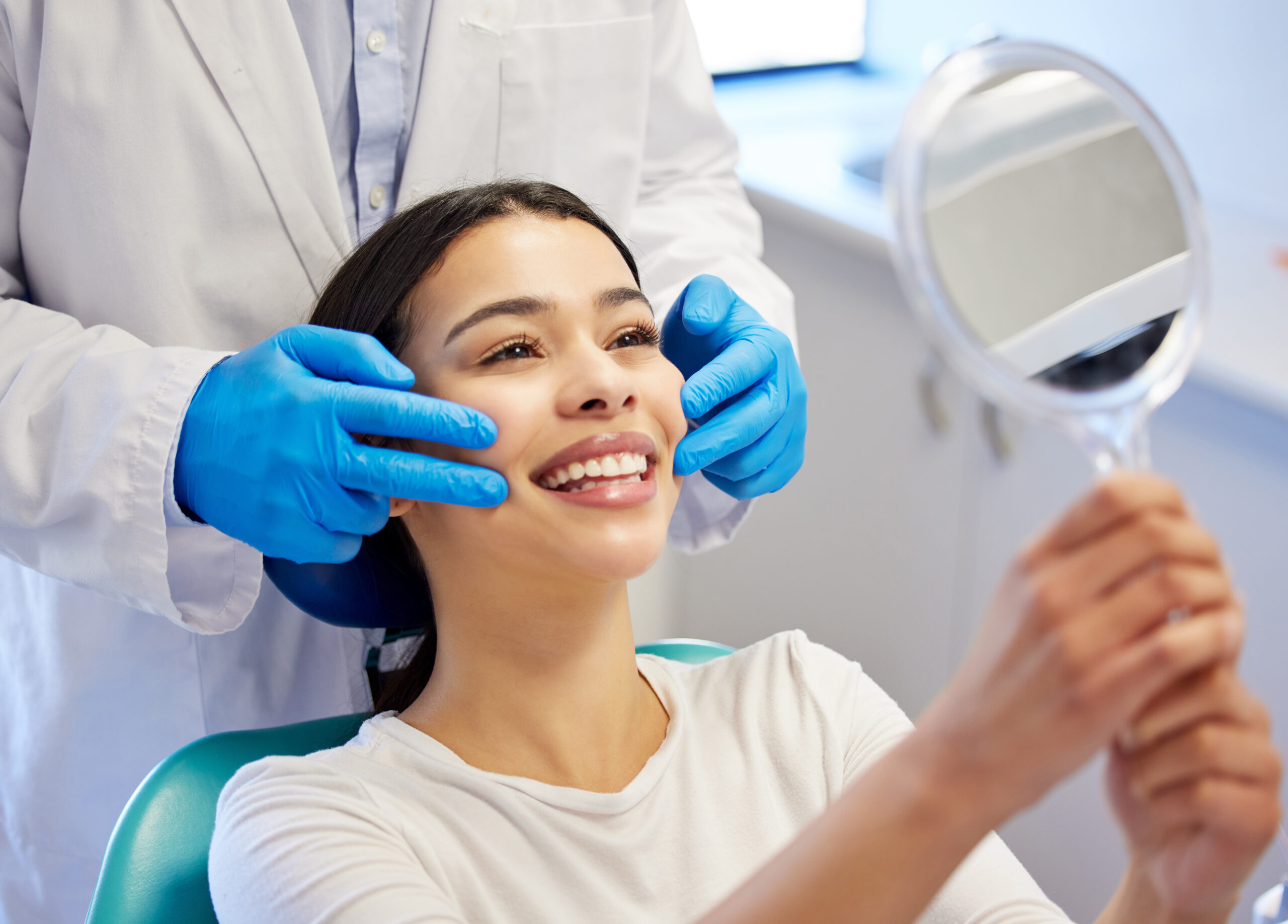 Patient smiling and checking her teeth in a mirror during a cosmetic dental visit for smoothing and improving tooth edges
